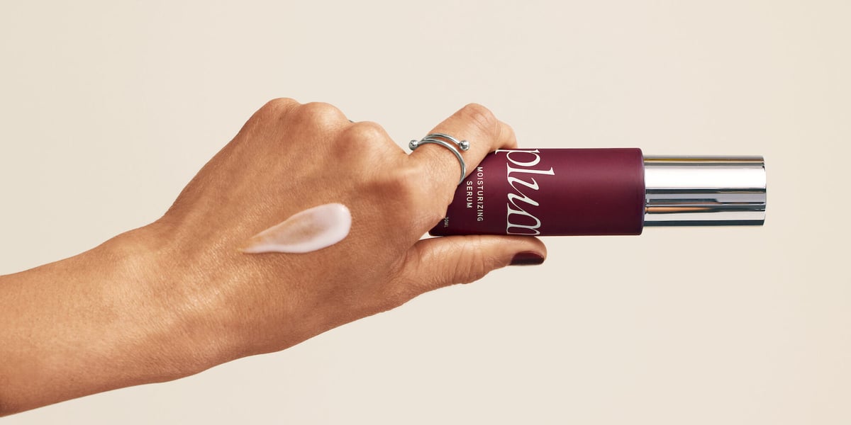 hand holds the plum bottle and has a smear of the product on their hand that is white and creamy. 